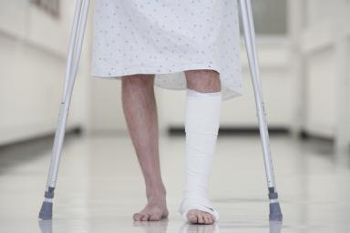 Close up of male with broken leg walking on crutches in hospital